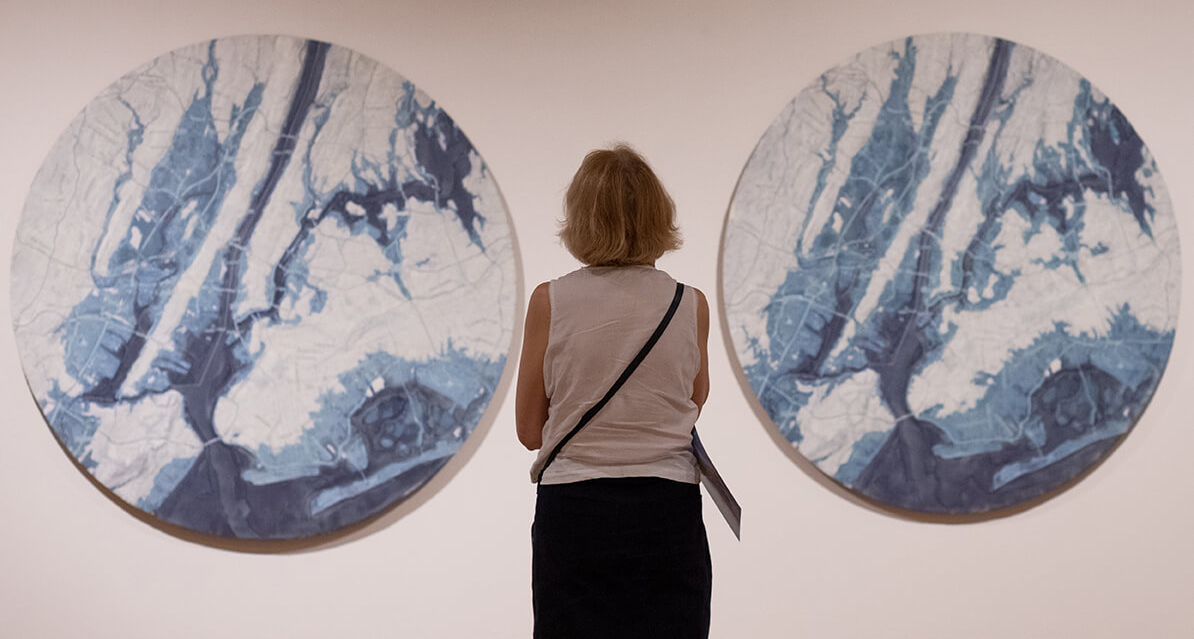 Back of a woman looking at two large circular flat blue and white artworks on the wall