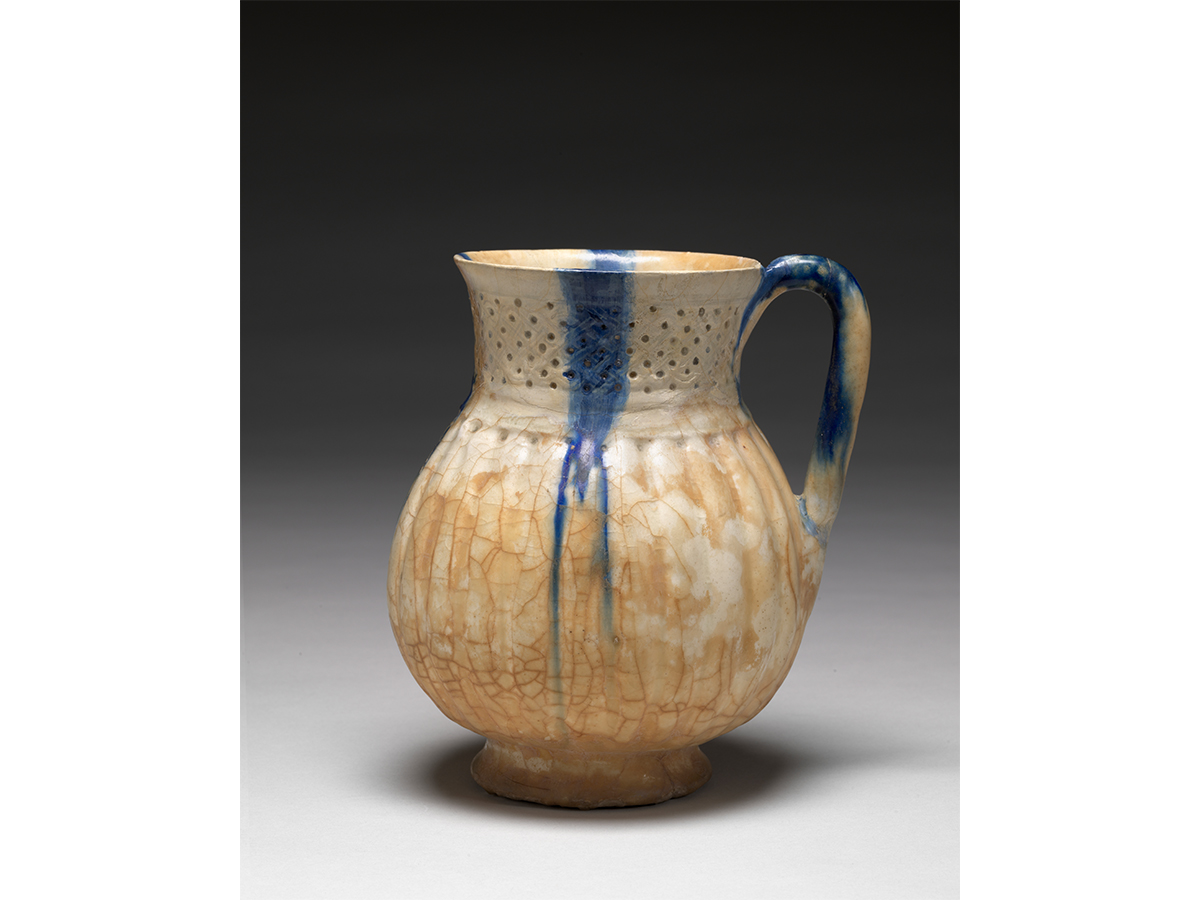Ceramic pitcher with crazed beige glaze foundation and thin blue stripe every 4 inches including some blue on the handle