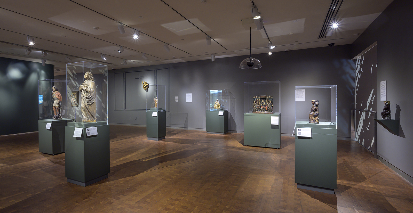 Long view of a gallery with painted wood sculptures on pedestals and on the walls