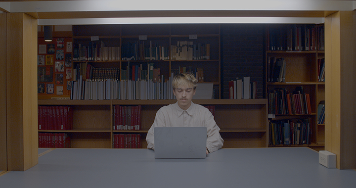 Person in library at a table with stacks of books in background