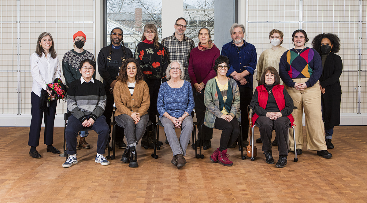 Two rows of 20 people, one row standing behind another row that is sitting in chairs