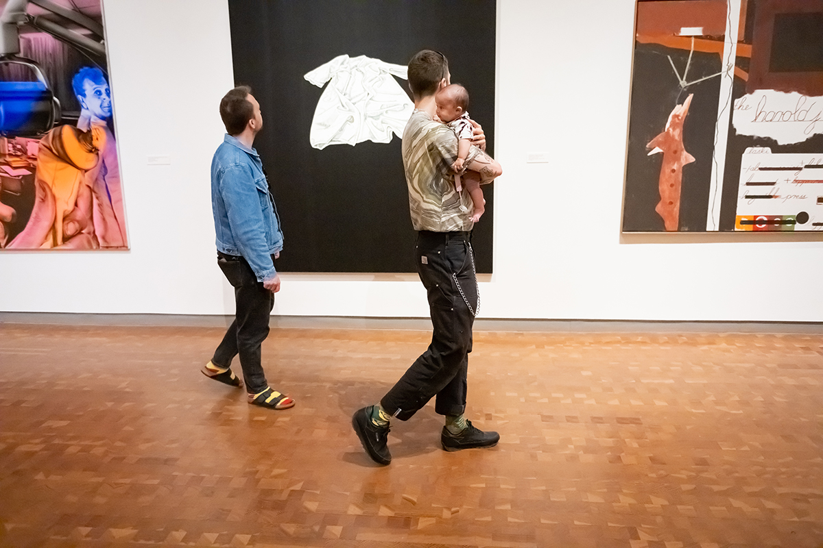 Two men and a baby in one of their arms walking in a gallery