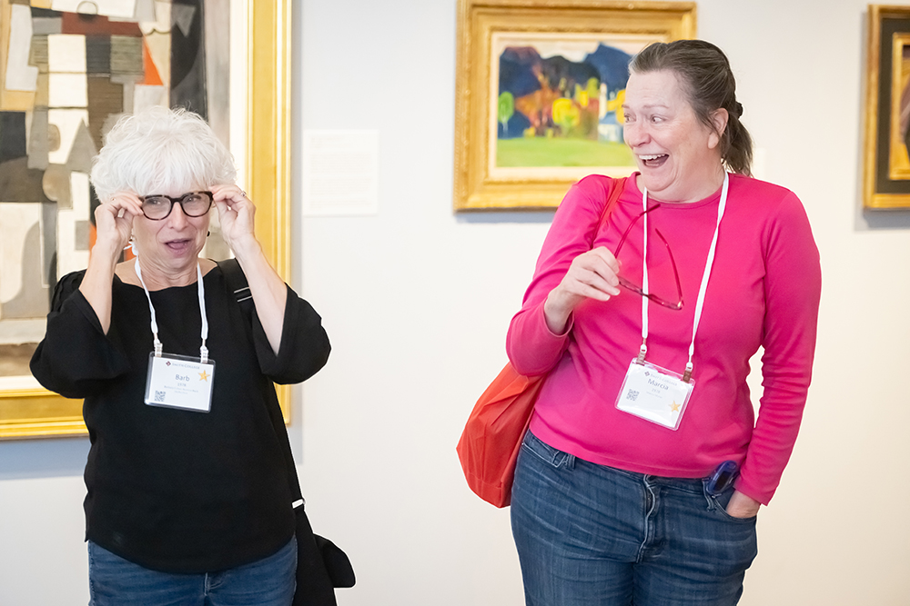 two older women smiling at each in an art gallery