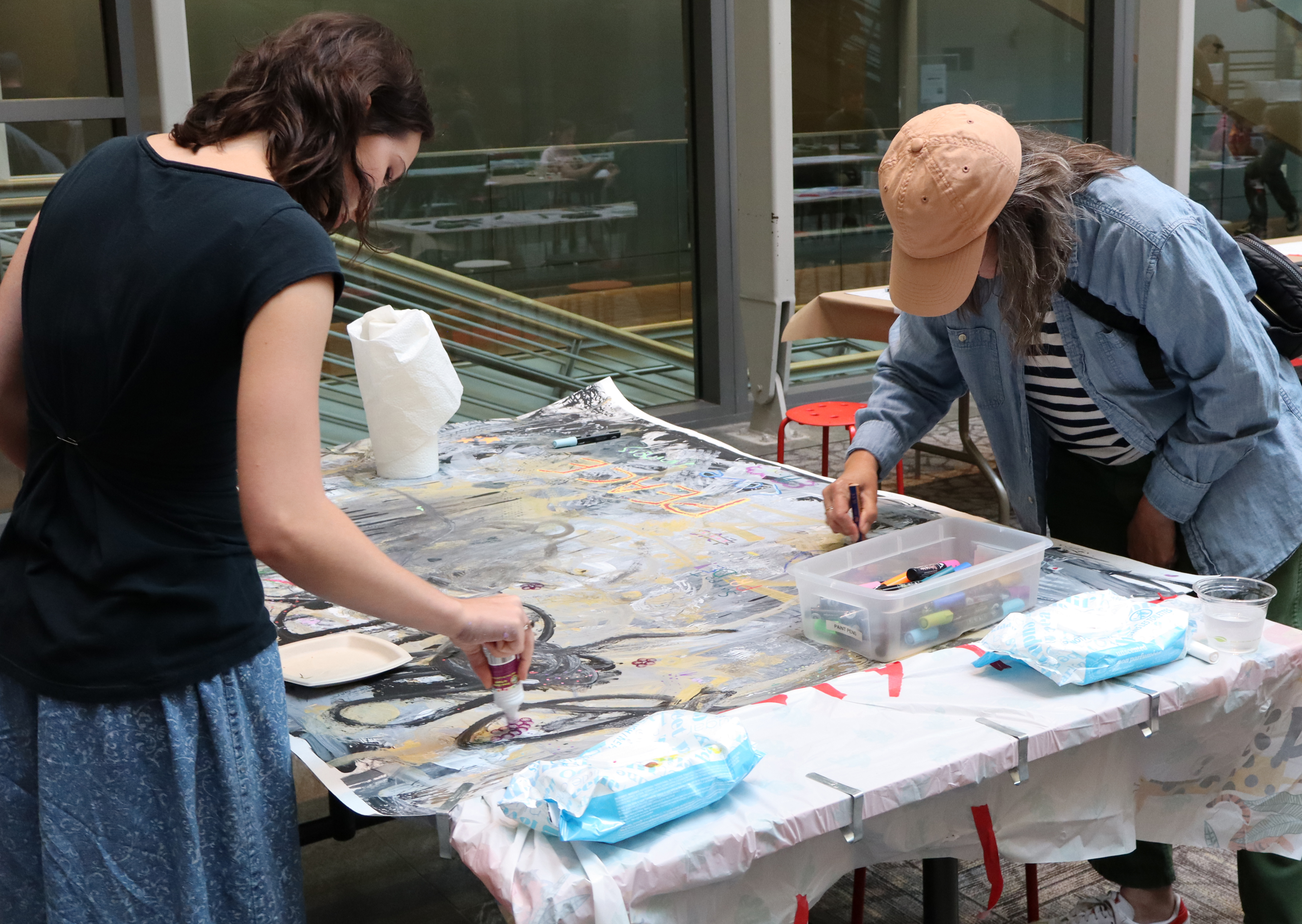 Two standing visitors working a a large art peice at the same table