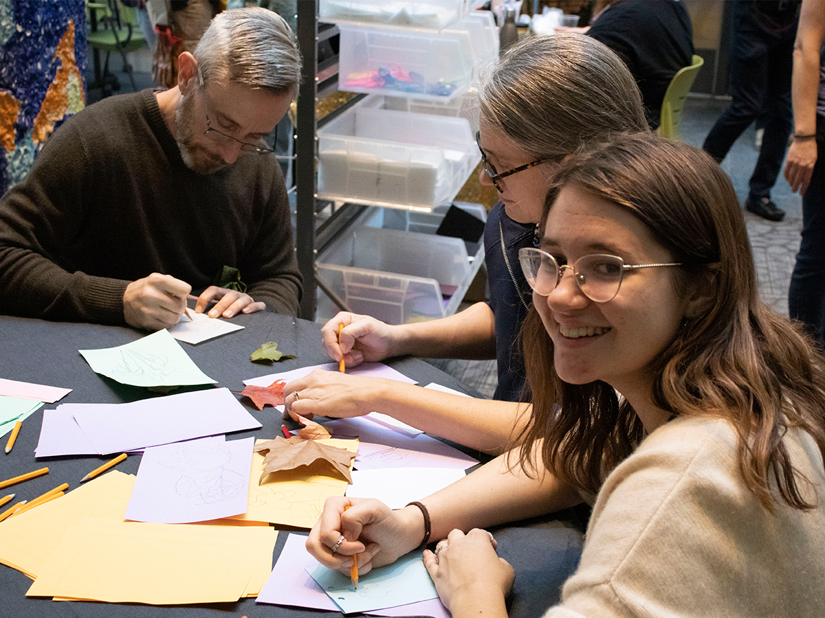 Two adults with young adult smiling at camera, all drawing at a table