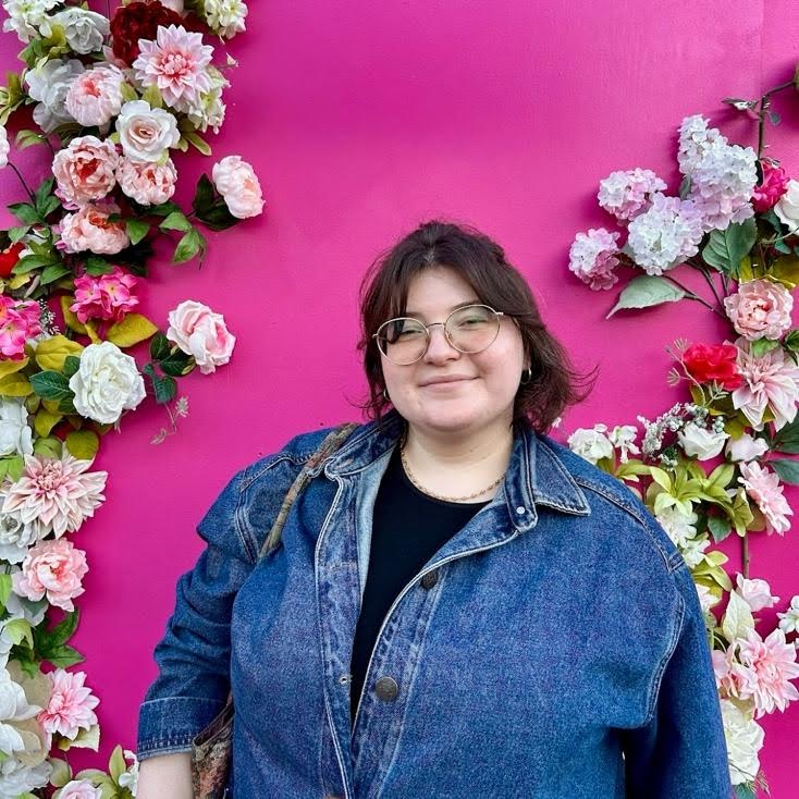 Olivia wearing a denim jacket with a bright pink background and framed with flowers.