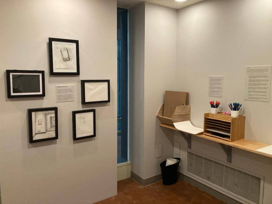 Cluster of drawings visitors to the museum made on the left and pencils and paper for drawing activity on the right.