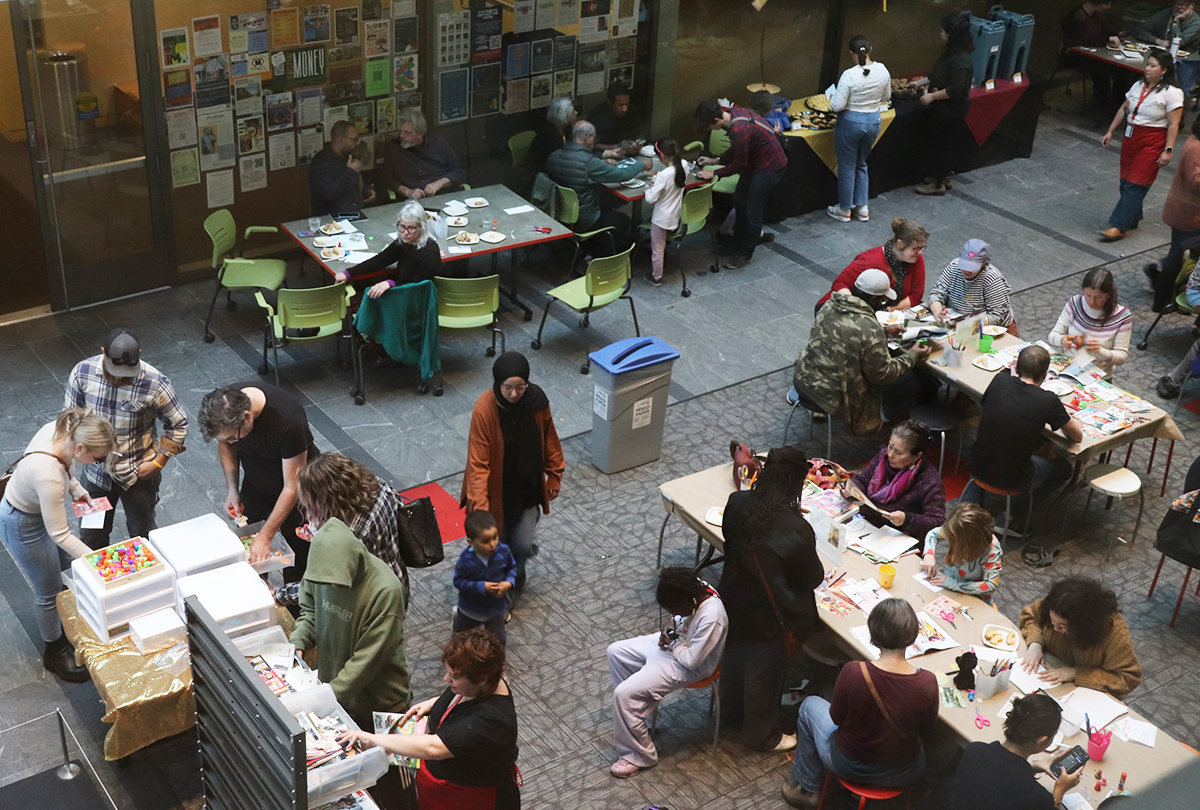 bird's eye view of an atrium full of about 32 people of all ages making art at tables and eating refreshments