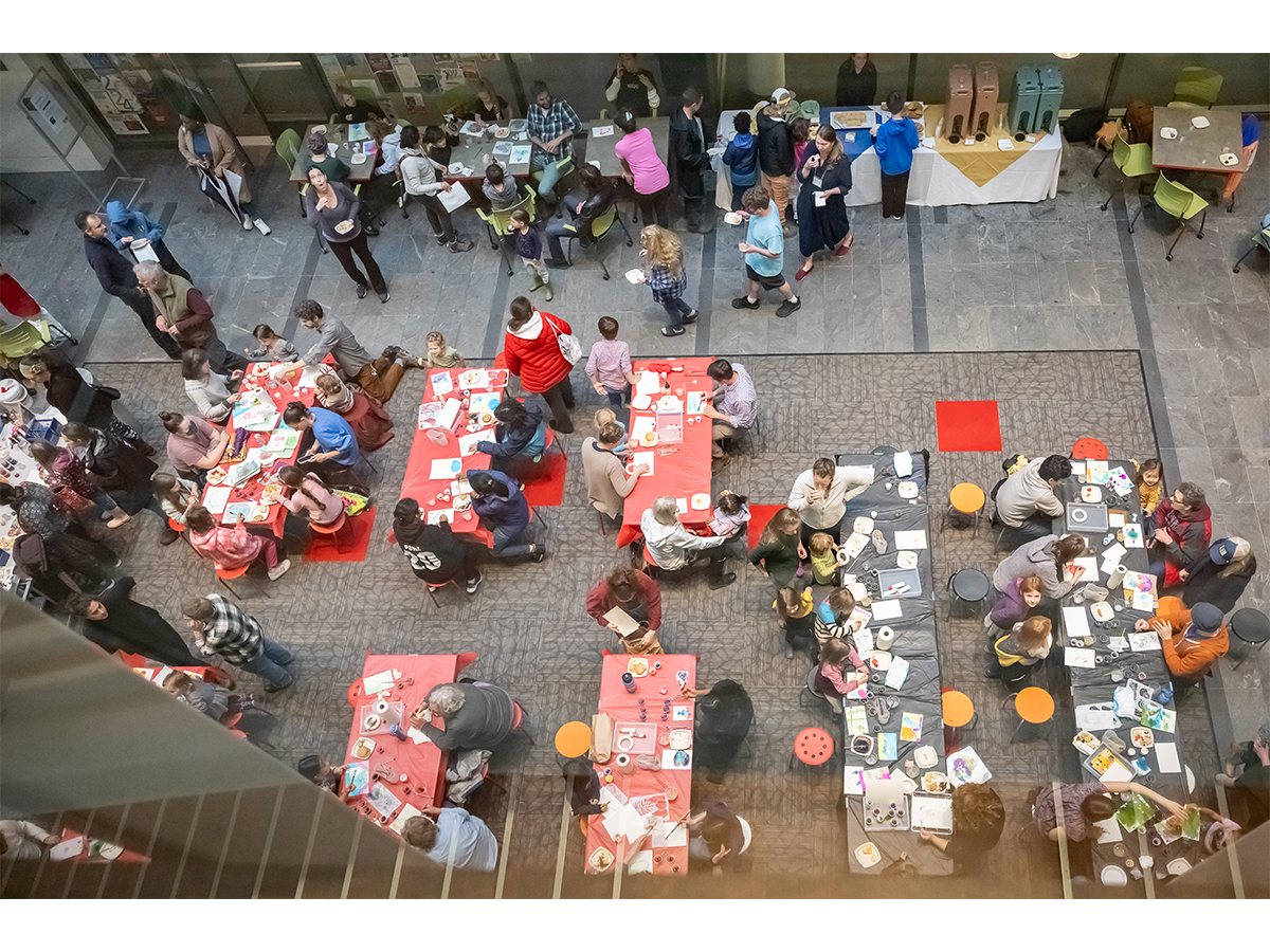 Birds Eye View of people making art at tables and eatng light refreshments together in one high ceilinged room