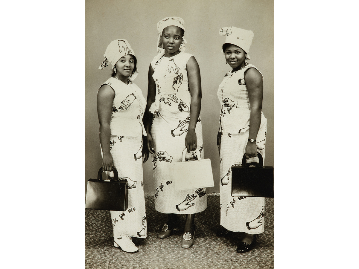 Three women in the same white dresses with hand pattern on them, all holding hand bags