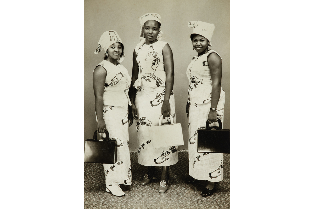 Thre women standing together in the same white dress, with hands on it, carrying handbags