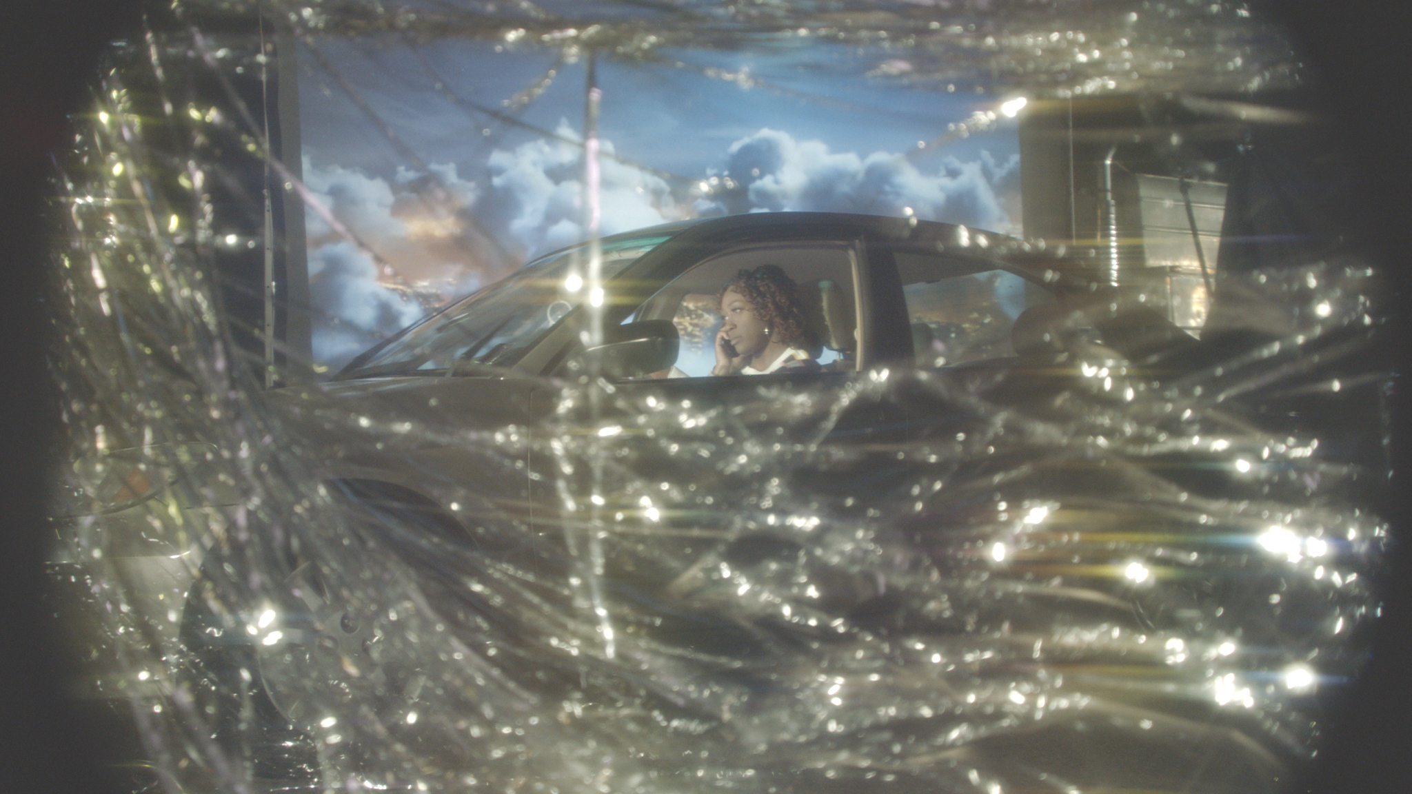 Figure in a car on the phone behind gold streamers