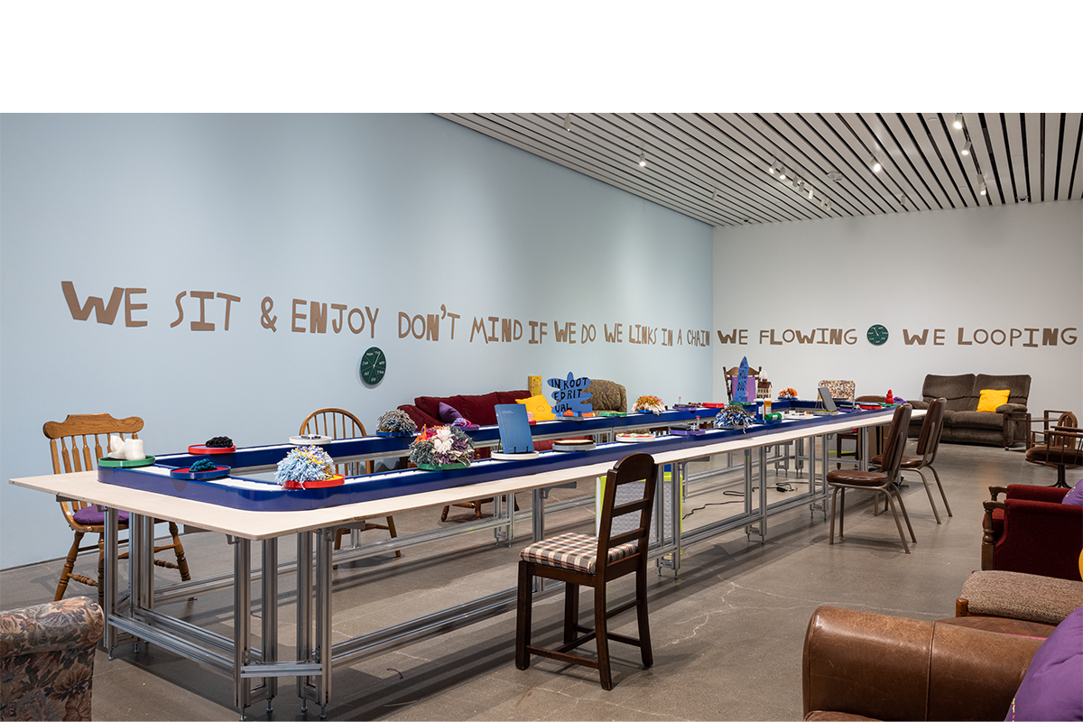 Photo of the exhibition featuring art from the show moving on a conveyor belt.