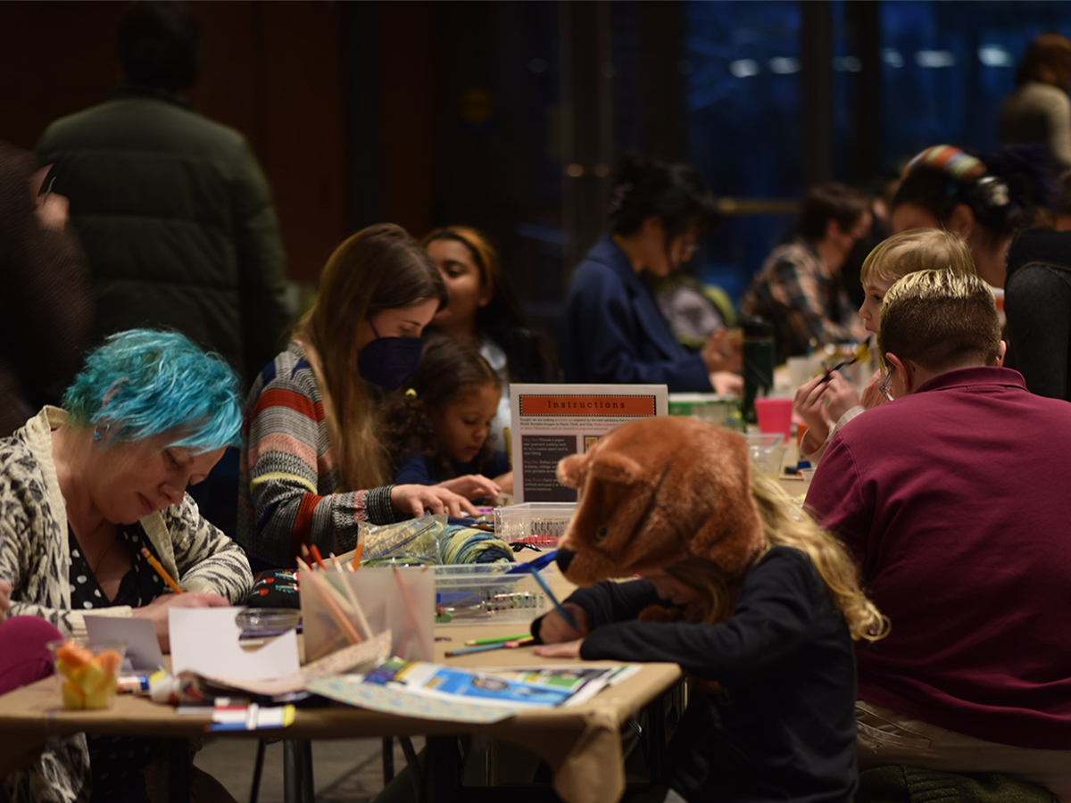 Group of people of all ages sitting and standing around a table and making art