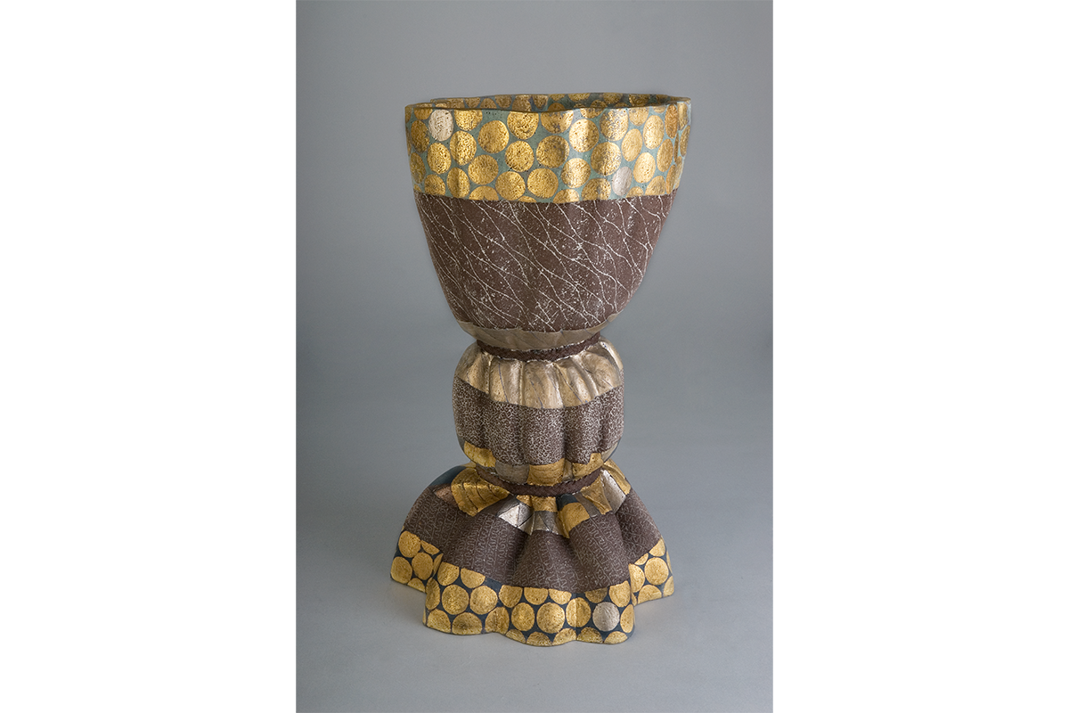 Goblet shaped stoneware with a texturized brown color and gold circle prints decorating the top and bottom of the piece