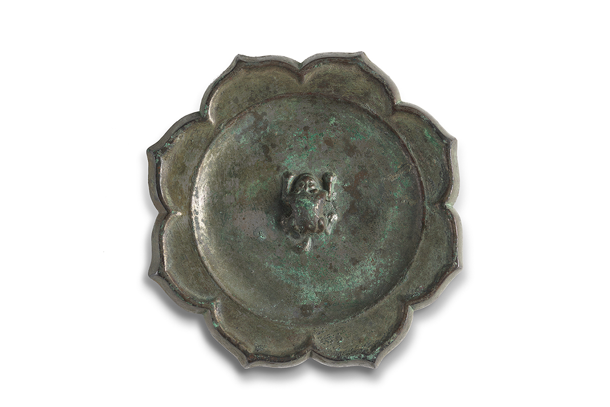 Circular dark bronze mirror with some green patina and eight wide and pointed petal shapes circling the edge. A small sitting frog protrudes from the center. 