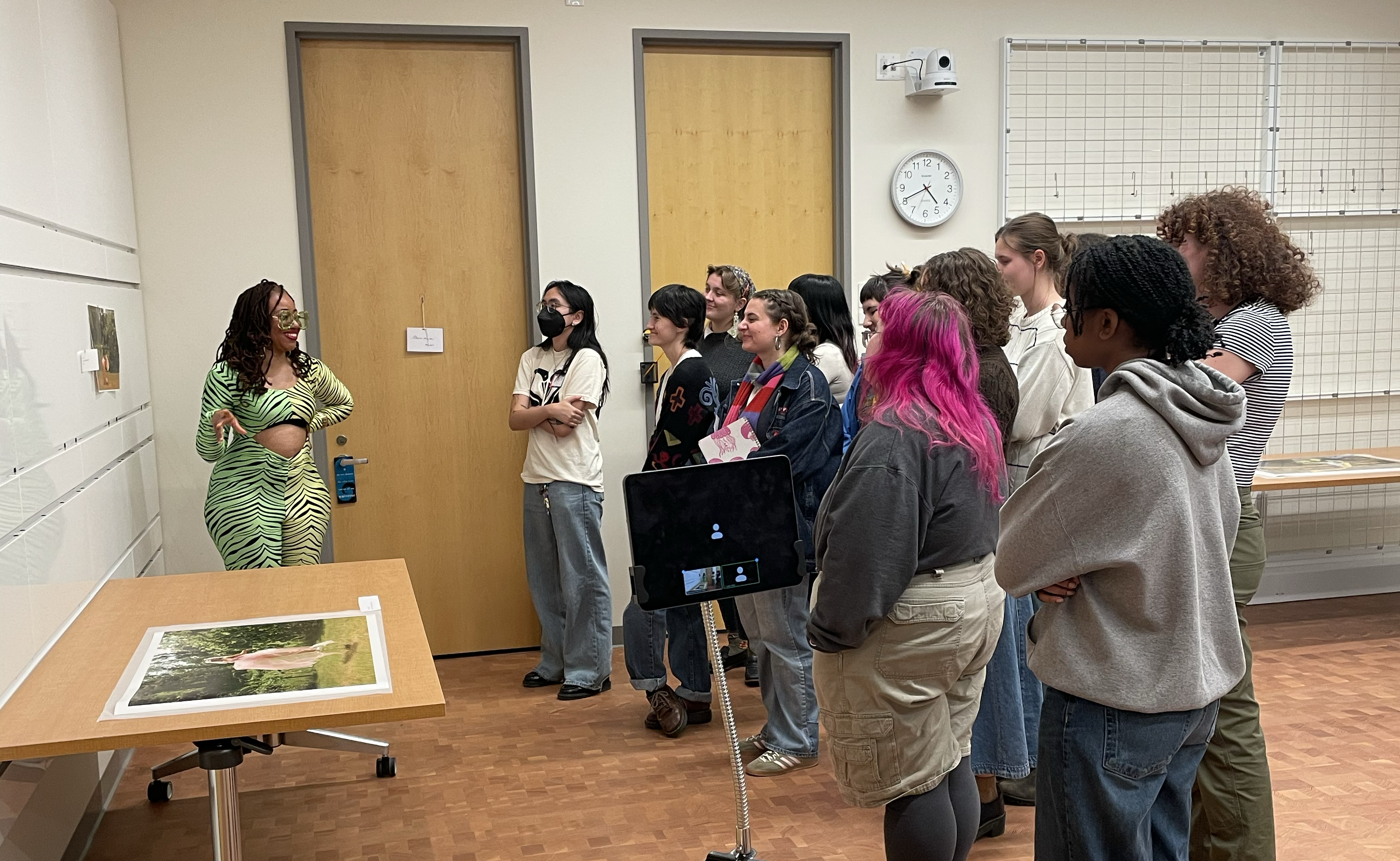 Artist on left speaking to a group of students with a print on a table