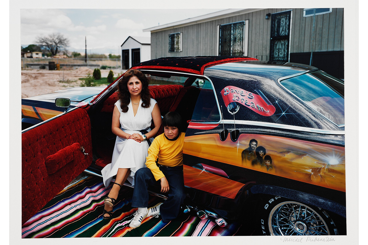 Person in a dress sitting sitting on the edge of a car seat with the door open and lined with red velvet and sitting with a young person 