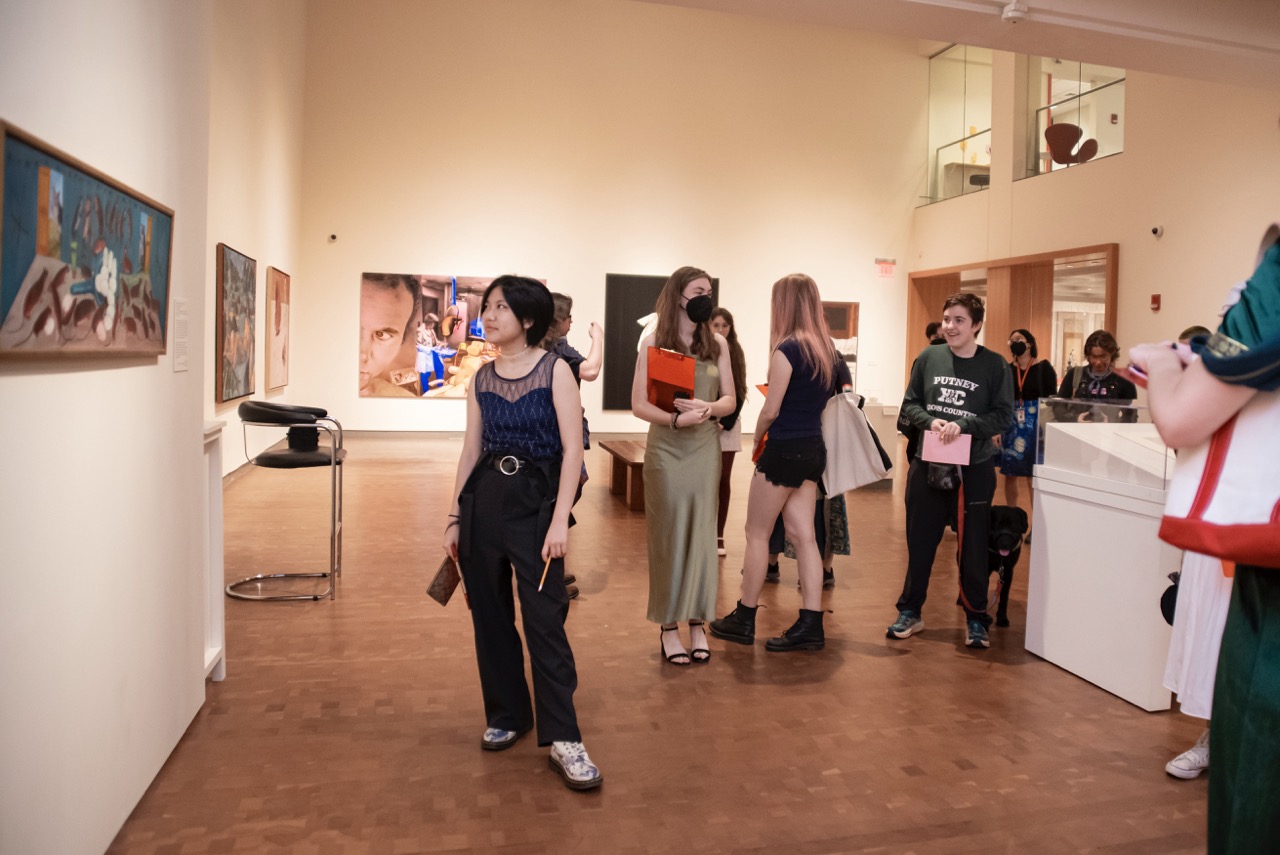 Group of students in a gallery dressed, holding clipboards and looking at art