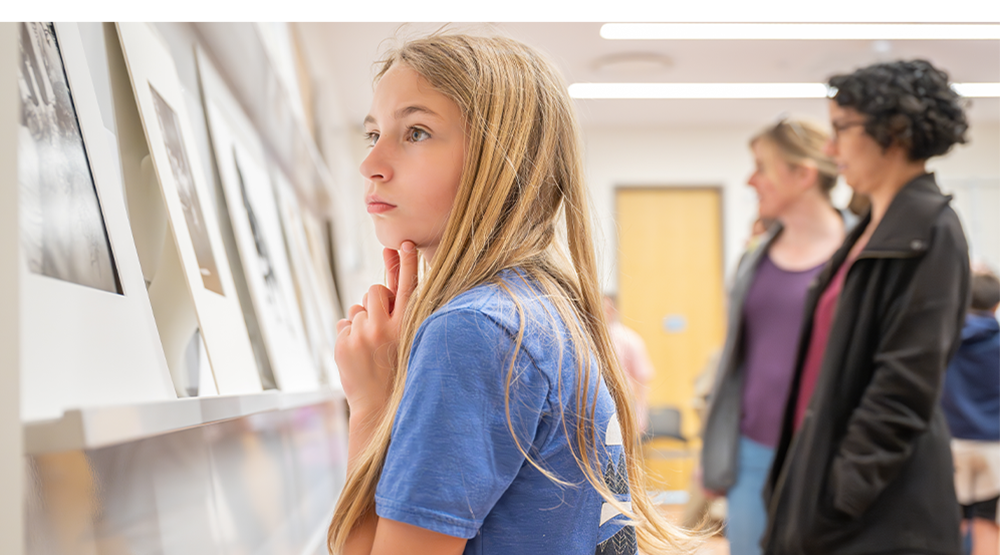 Young person looking closely at an artwork with 2 people in the background