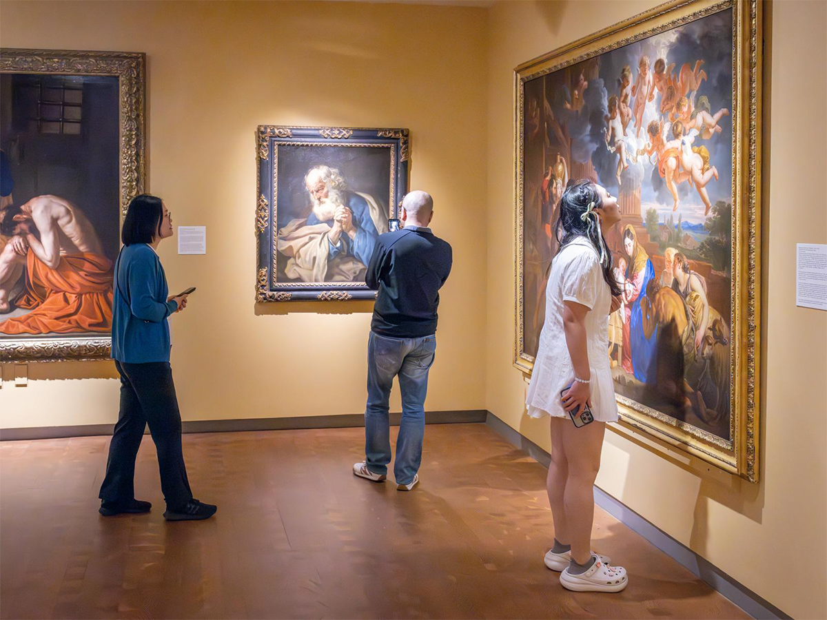 Three people in a gallery looking closely at art on the walls