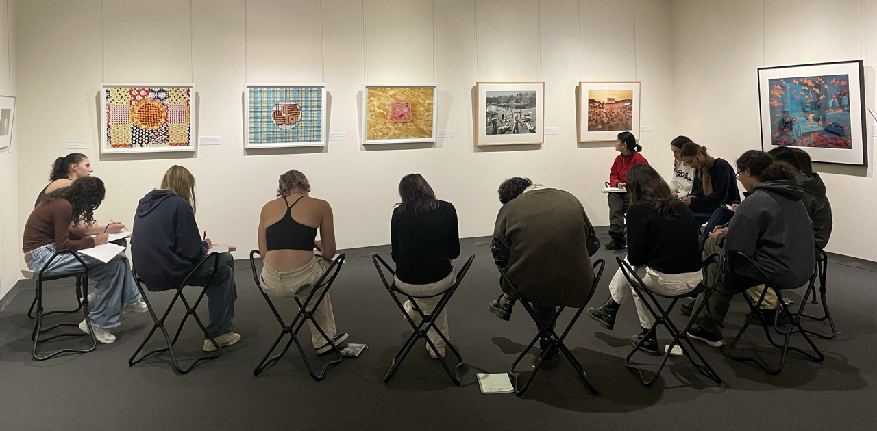 11 People sitting on gallery stools looking at 6 artworks hanging on the wall