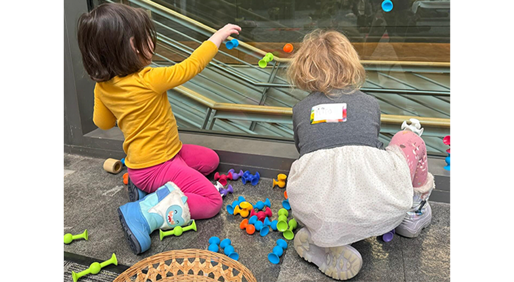 Two young preschoolers playing with suction cup toys on a glass window