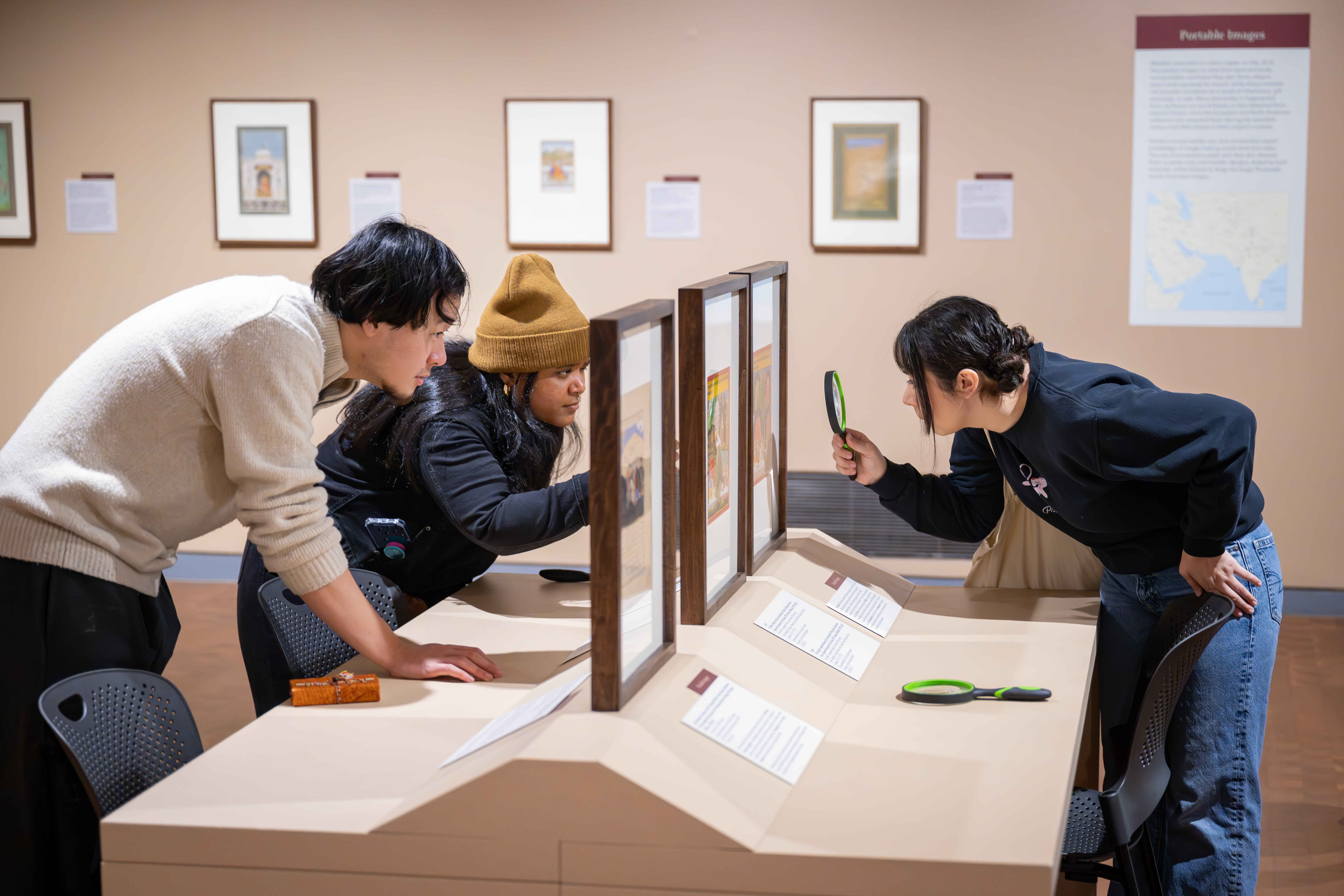 Three people engaging with a work on art closely with magnifying glasses