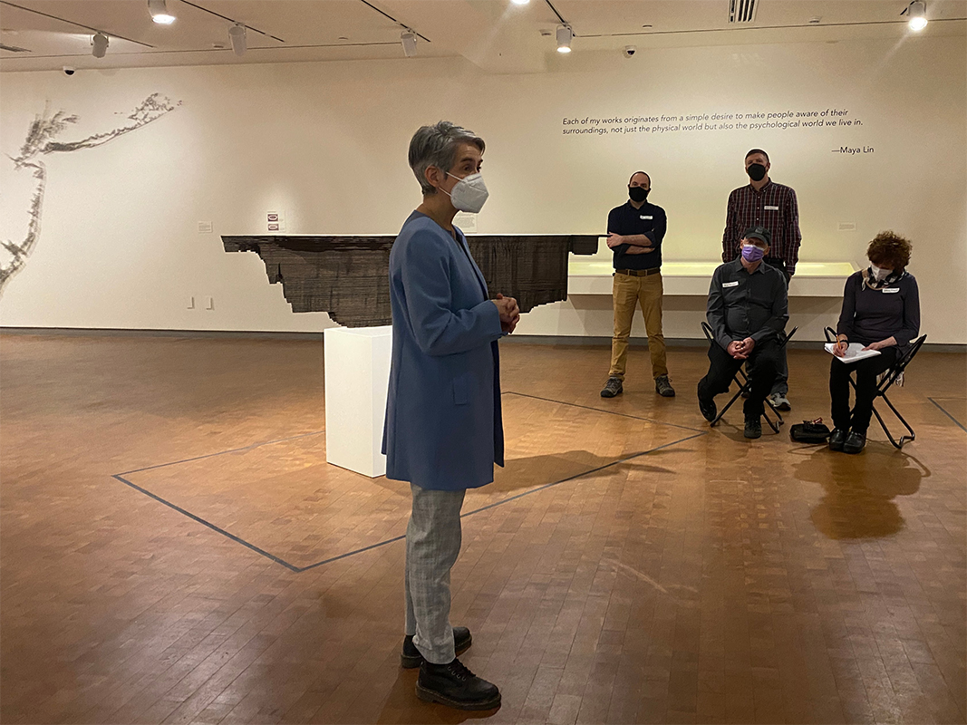 "Woman in periwinkle standing in front of group of adults in the Mappings exhibition"