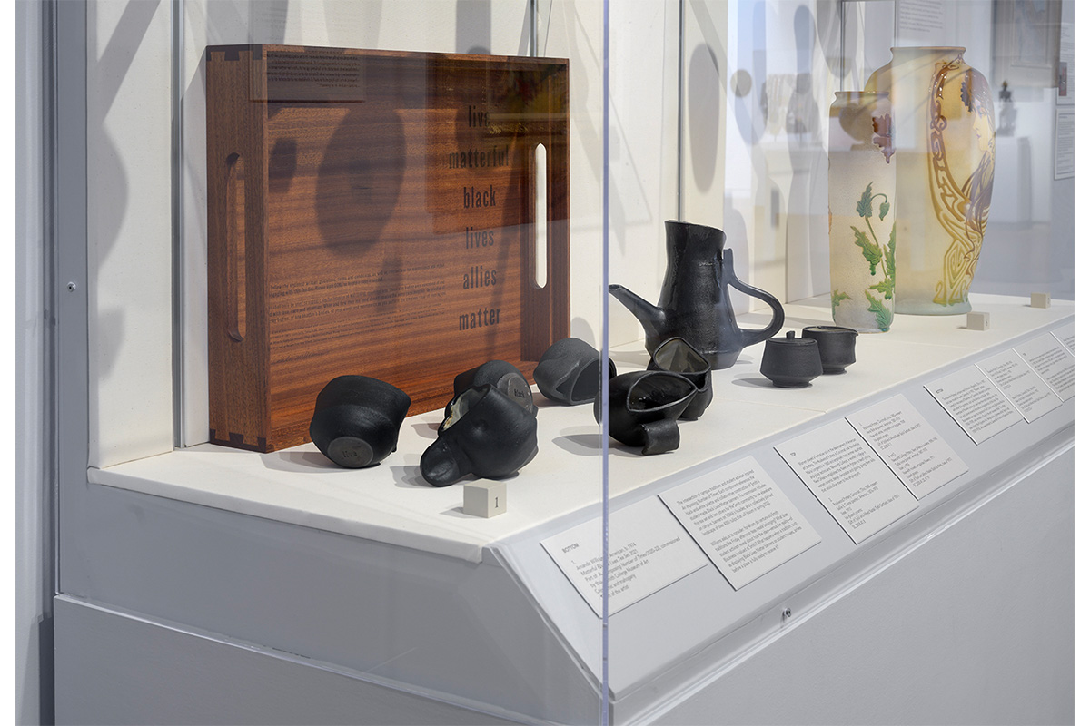 "Black tea set in glass case in front of dark wooden tray which is inscribed with 'matterful black lives allies matter'"