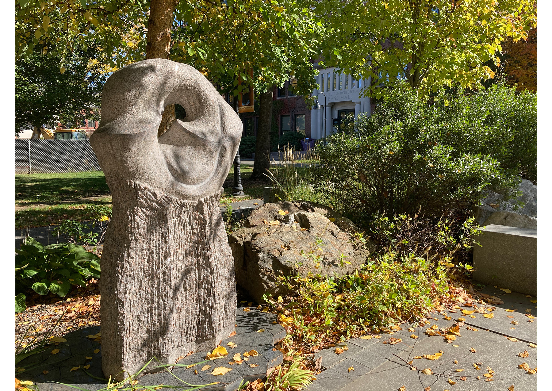large gray stone sculpture composed of rectangular base and circular top, standing among various leaves and rocks