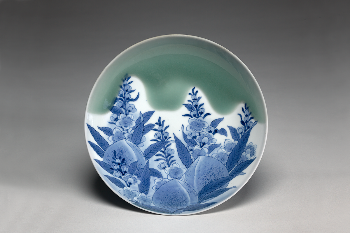 Plate displaced upright with blue drawing of peaches, leaves and flowers with a green glaze background