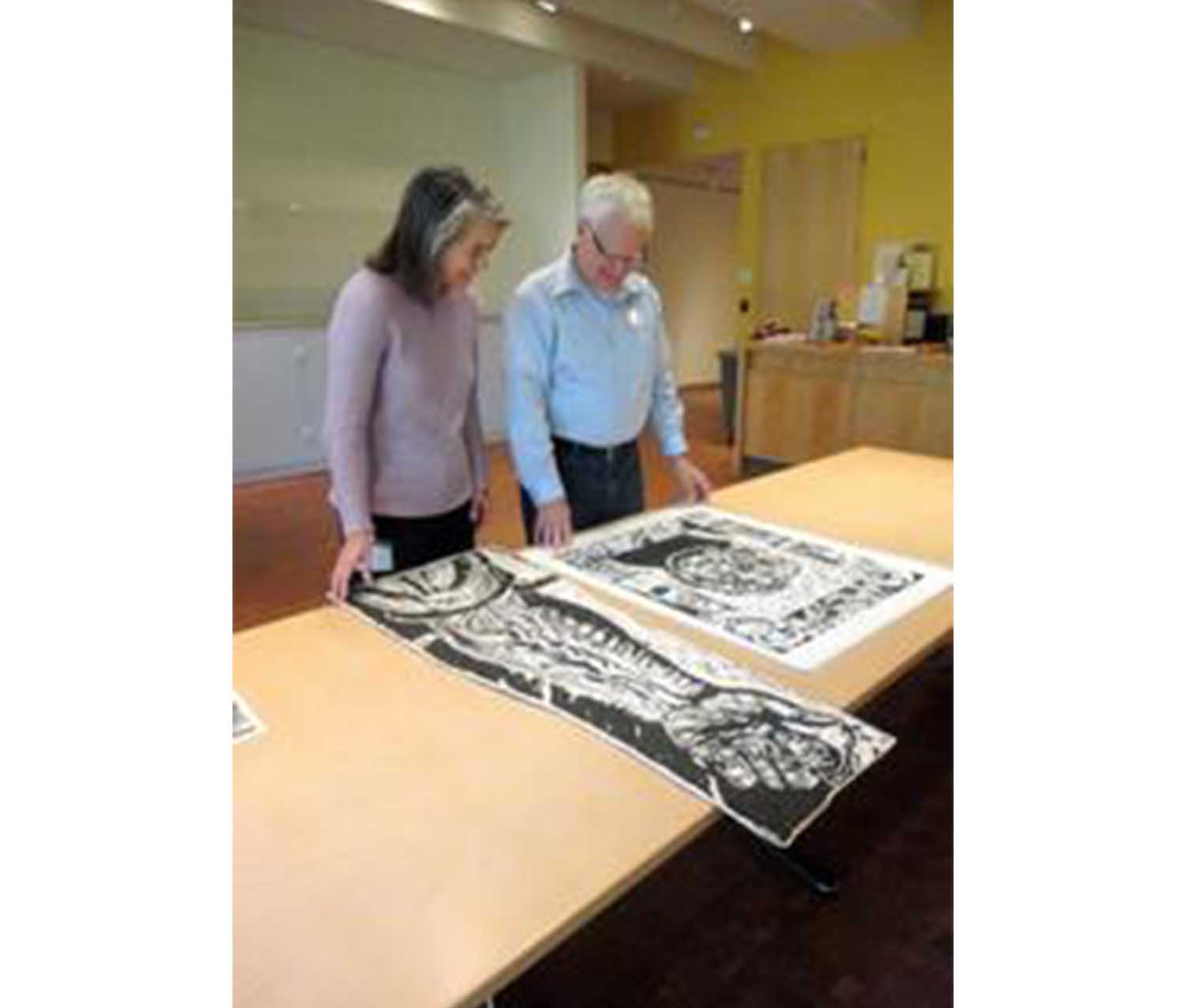 woman and man standing over a table, looking at two large prints