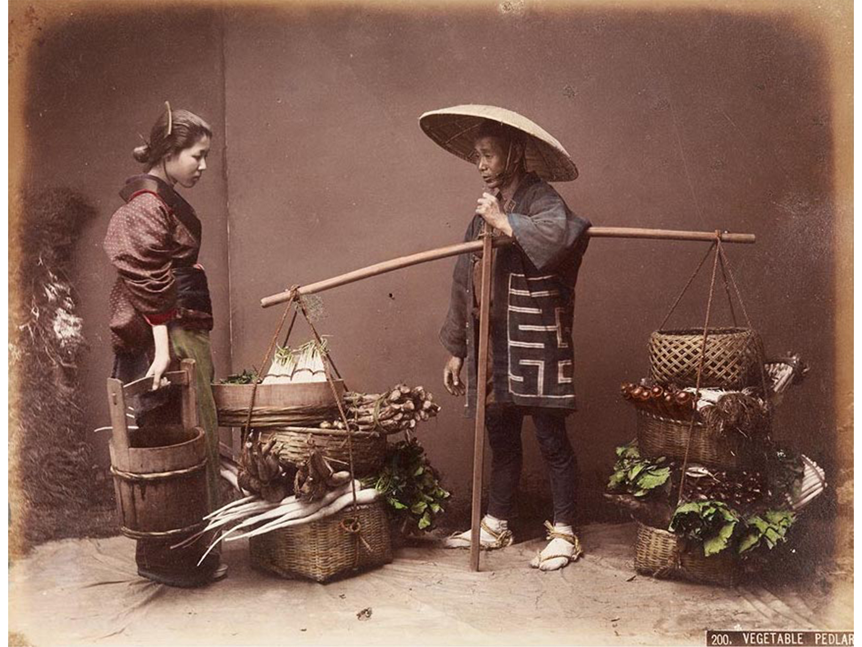 interior, two figures standing, at left a young woman holding a water bucket, at right a man with coat and large hat holding a pole from which hang two stacks of three baskets at each end, filled with vegetables