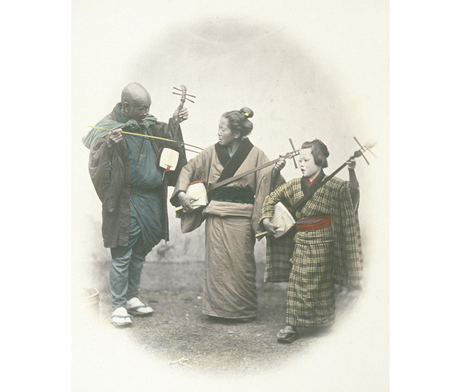 three musicians in shabby traditional Japanese clothing; an older man and woman and a young girl playing string instruments (Shamisen)