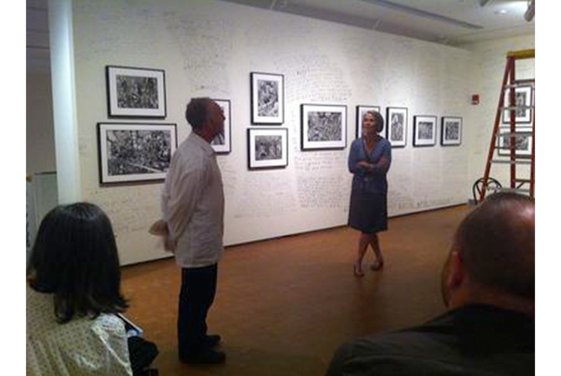 art gallery with prints all along the walls; man and woman stand in front of an audience