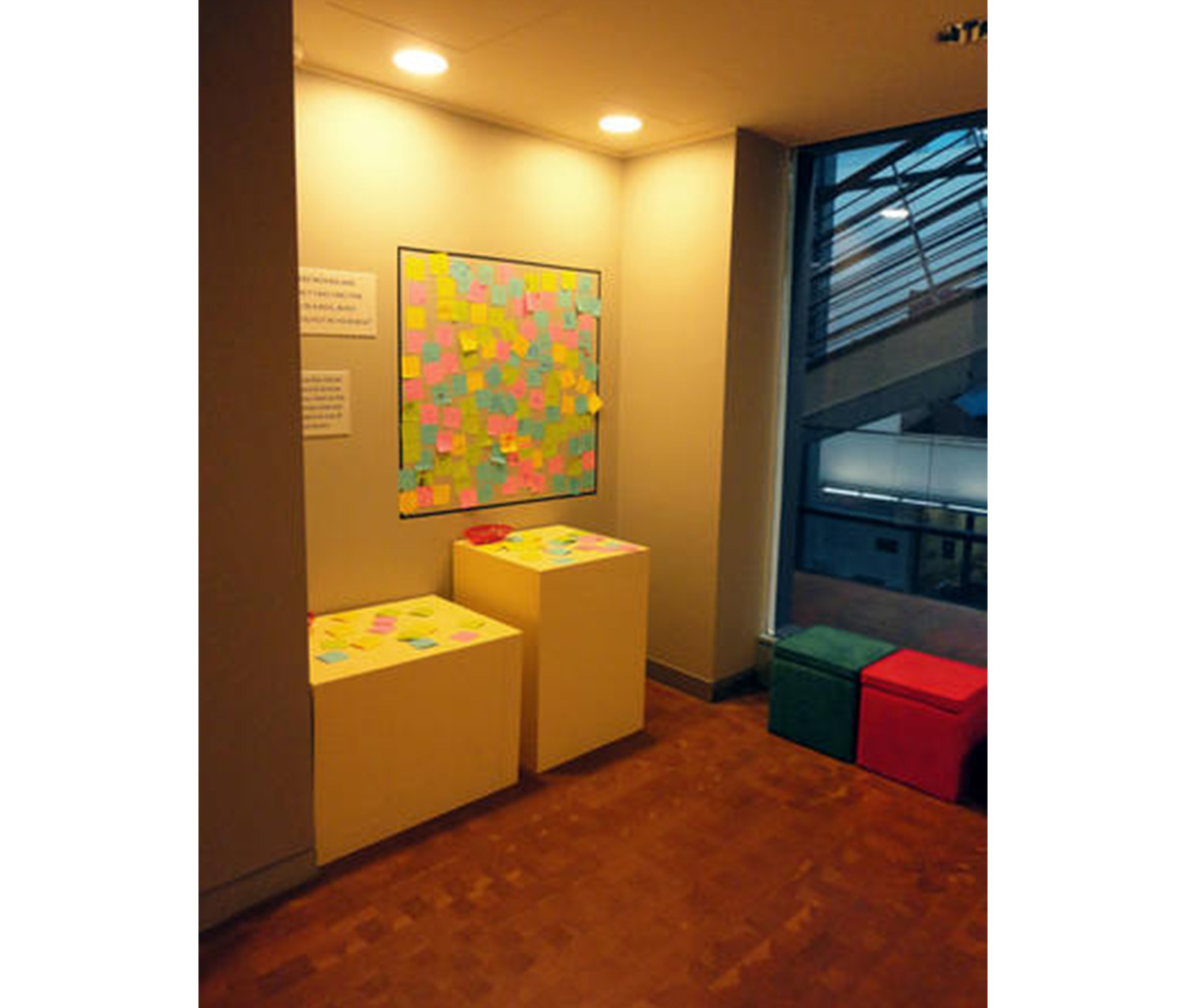 wall covered in colorful sticky notes. two countertops underneath the wall display with sticky notes and pens laid out on them