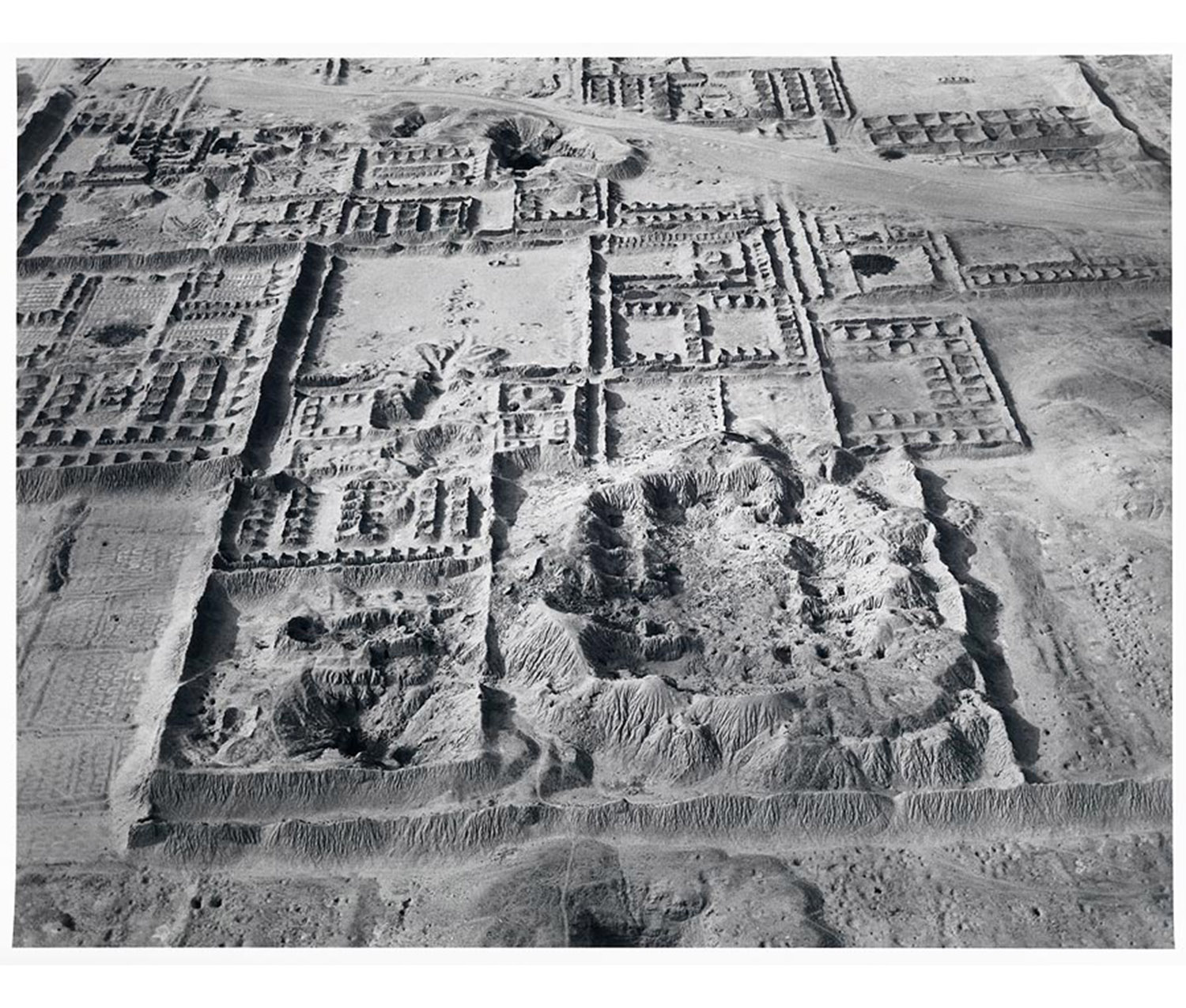 aerial view of sandy area with low dirt mounds and rectangles of ruined buildings