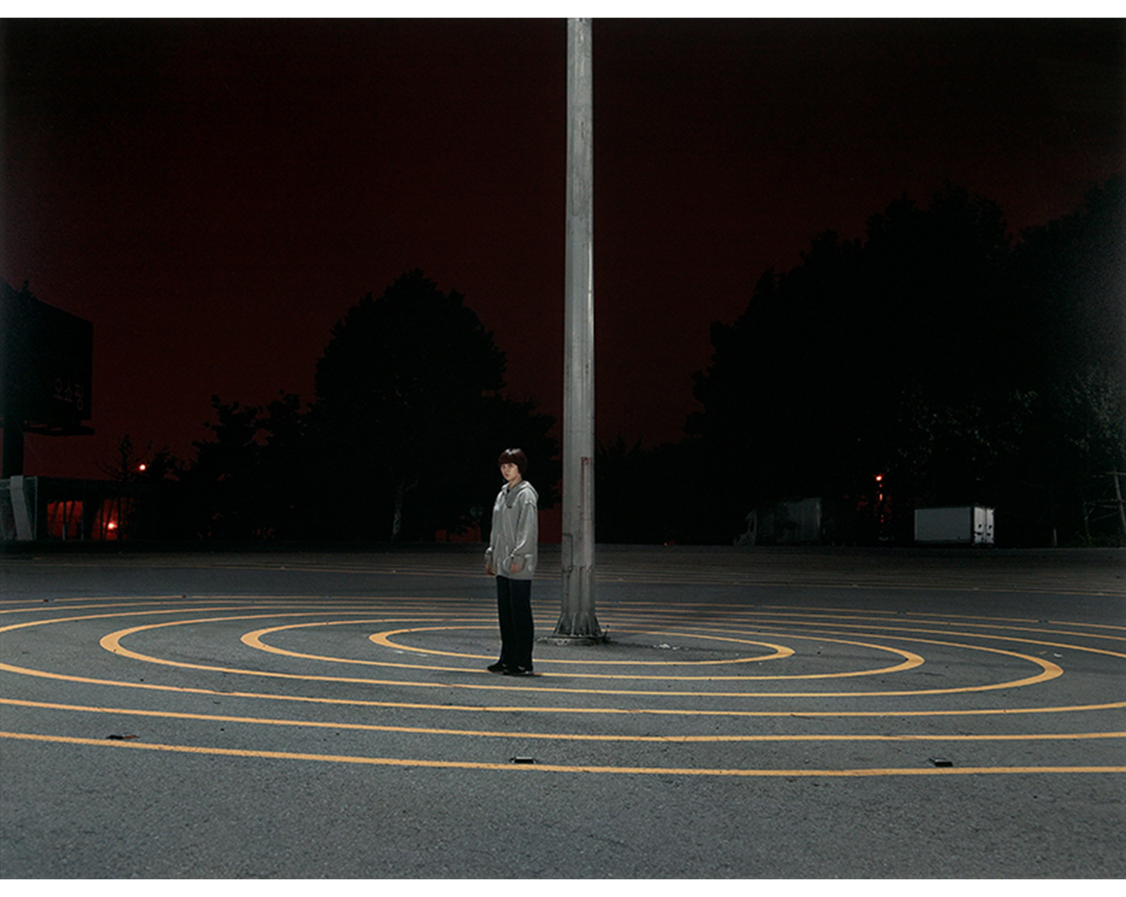 night, boy standing near a pole in the center of a series of yellow concentric circles