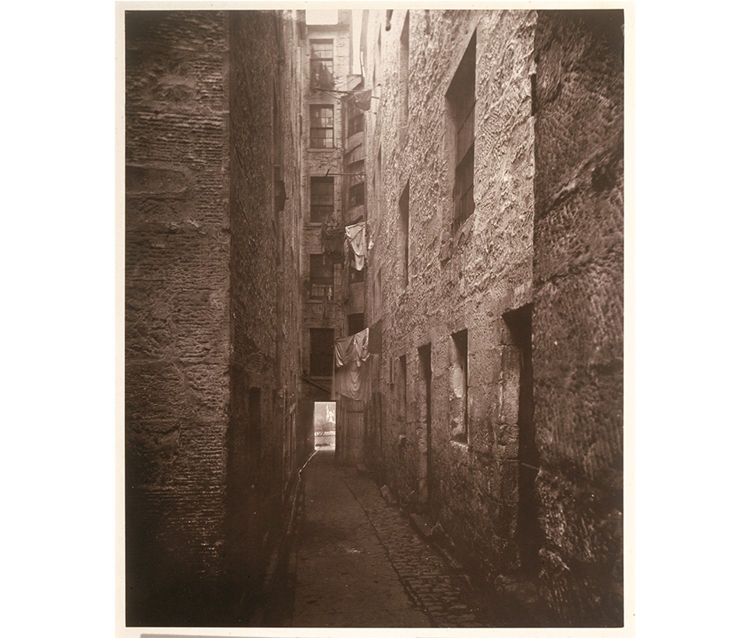 outdoor view of a small alley between brick buildings. clothing hanging on lines from some of the balconies