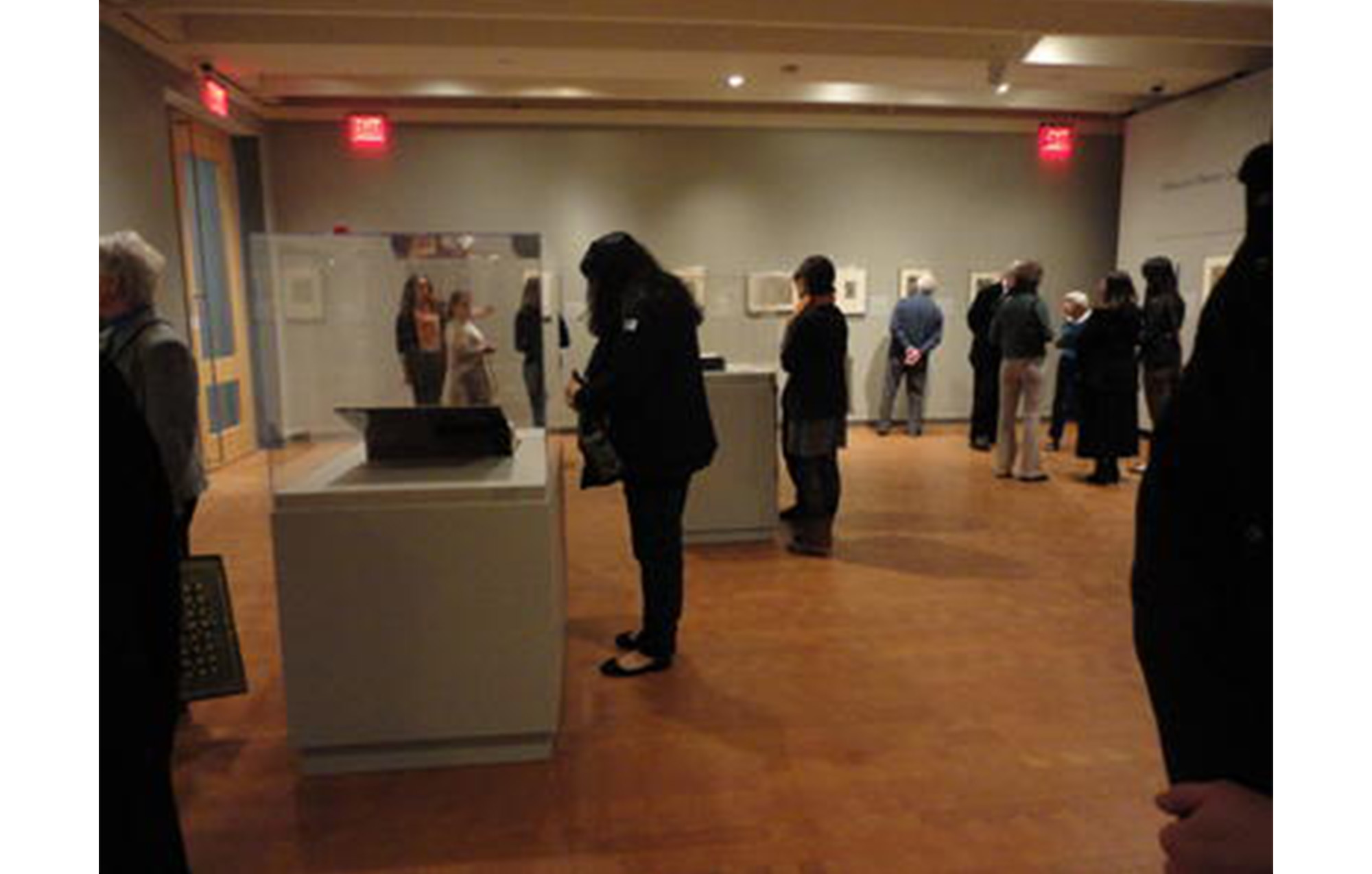group of people looking at objects in display cases in an art gallery with prints hanging on gray walls