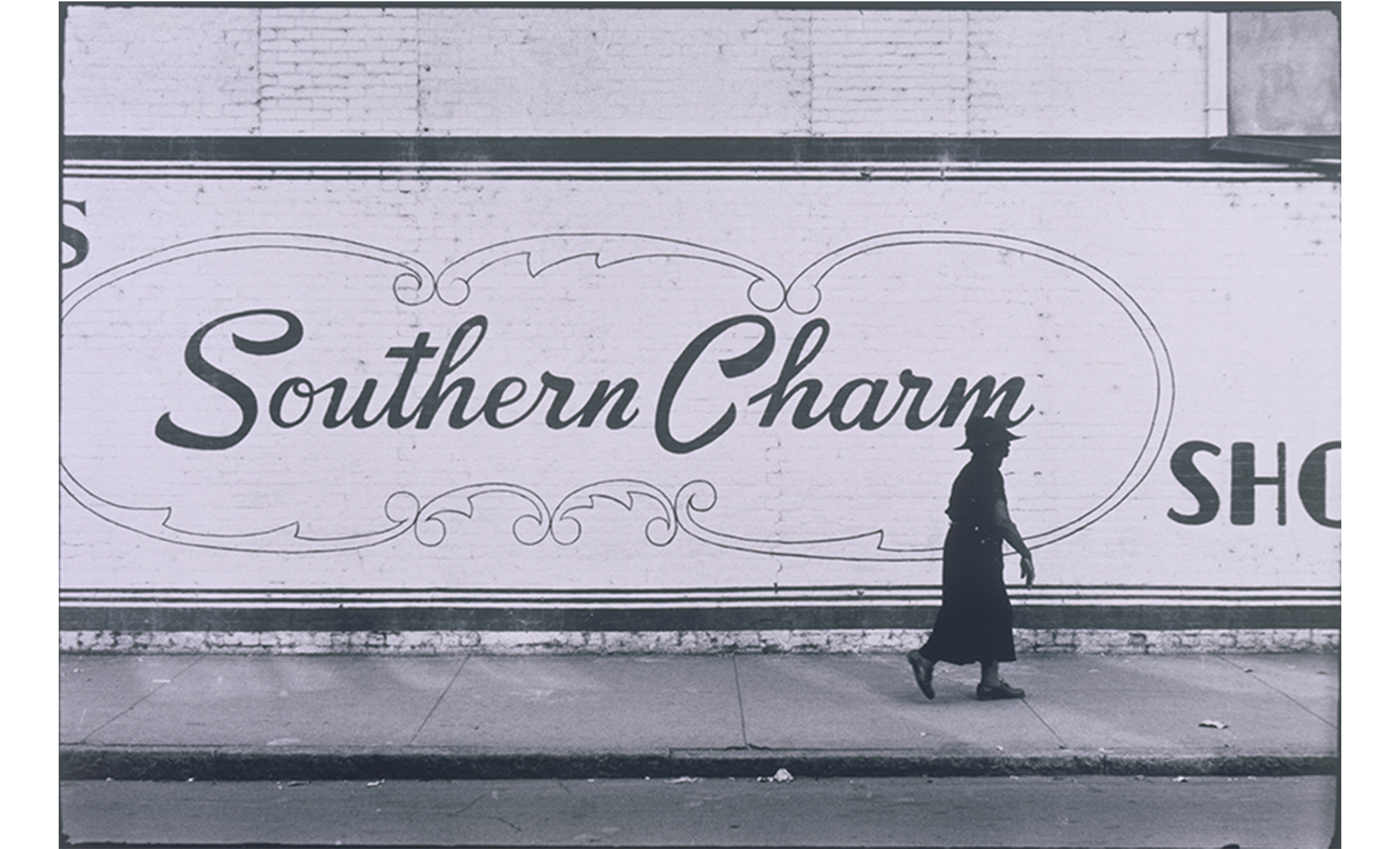 billboard-like sign on street saying "southern charm" with woman walking in front of it