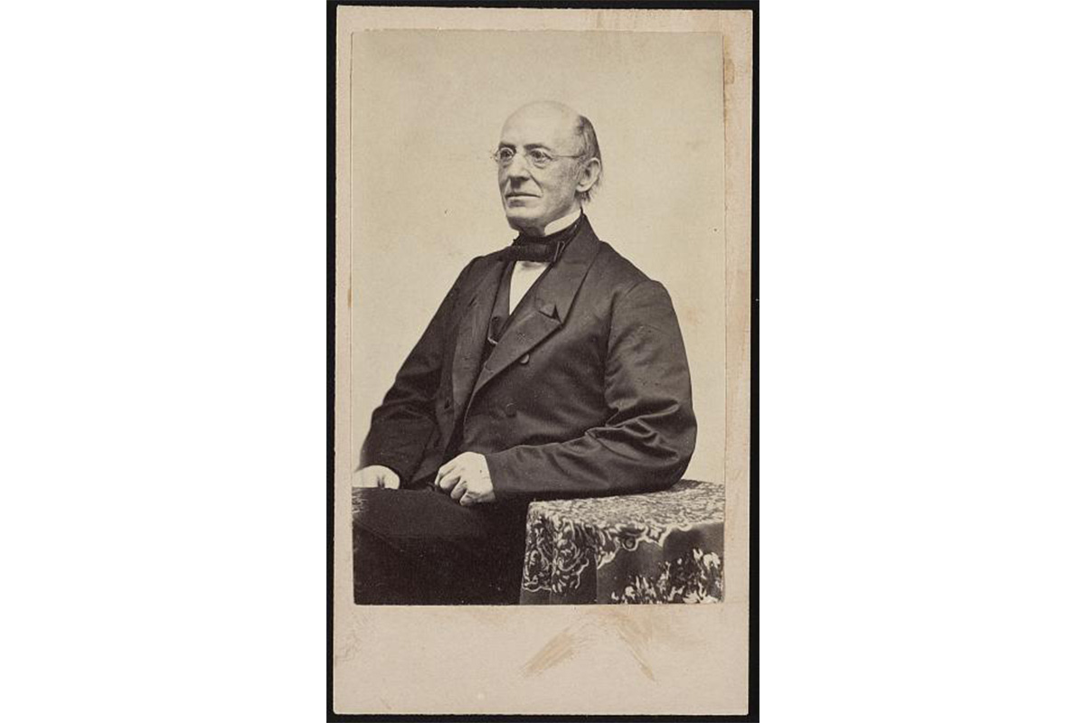 "Seated older white man facing left and resting his arm on a side table covered with a decorative cloth"