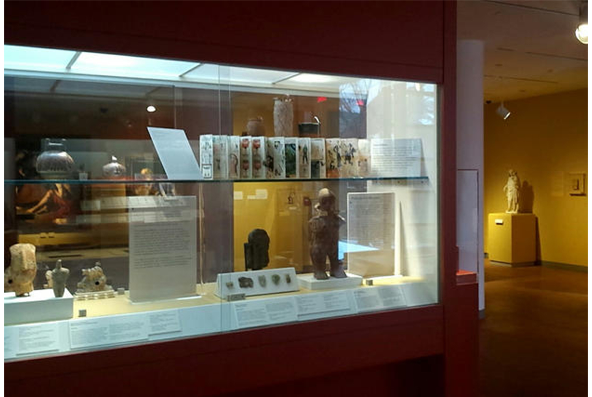 museum gallery. glass display cabinets embedded in dark red walls. artworks inside the cabinet.