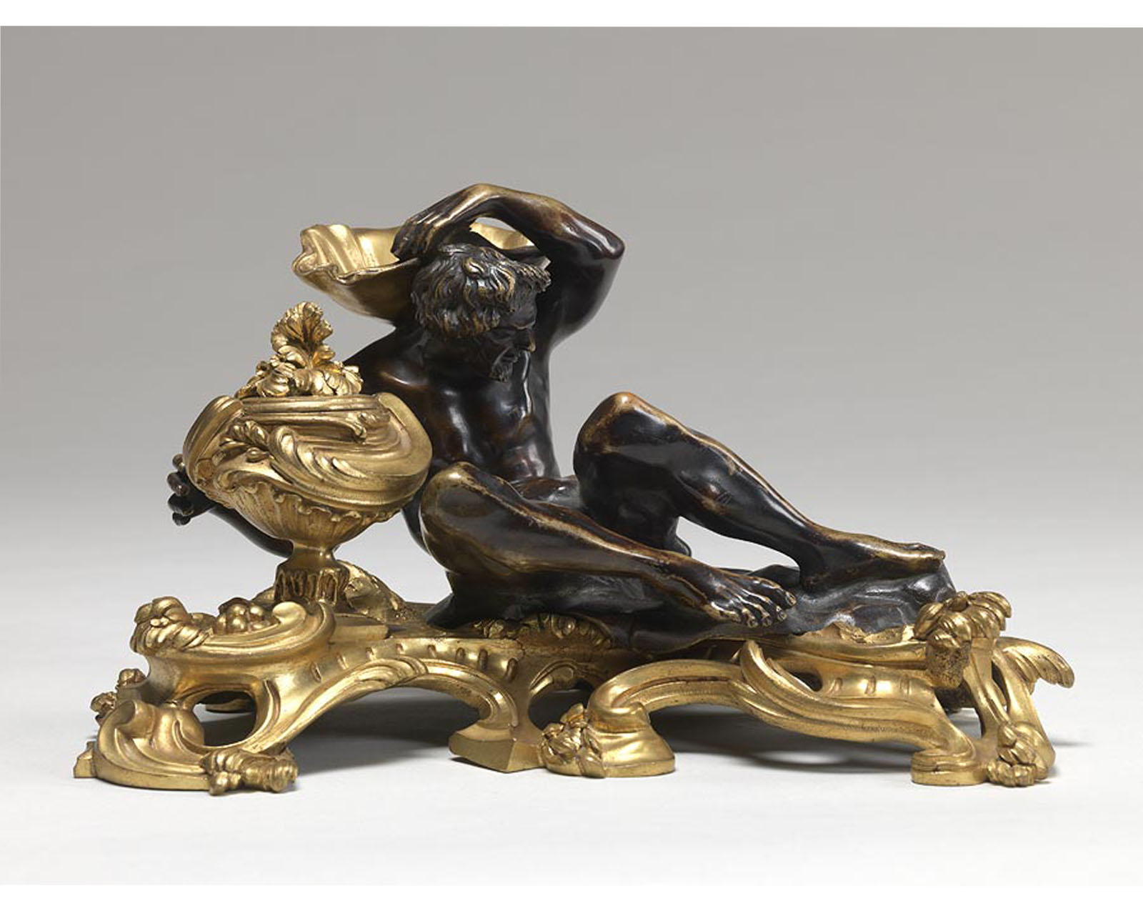 gold platform with a reclining male nude on top, reaching his hand into a pot in which one can place ink