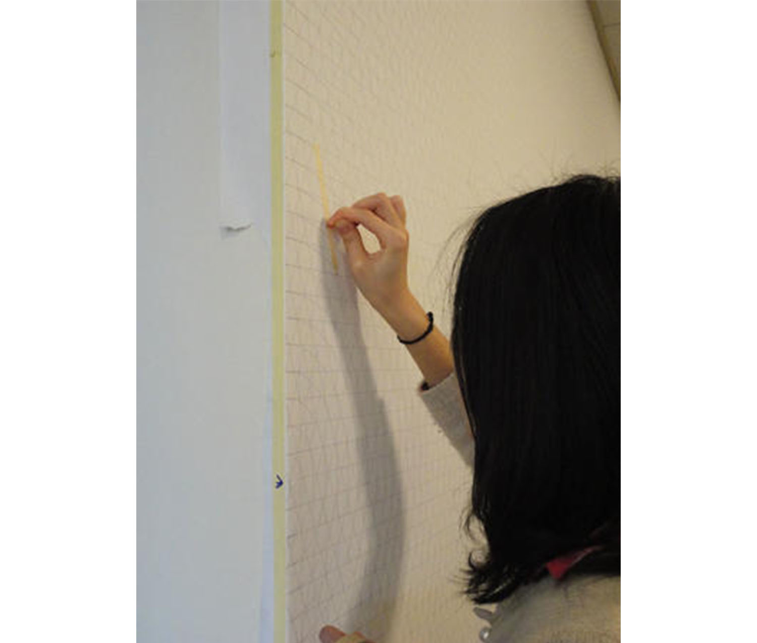 view of the back of a girl's head; girl is holding a small pencil and drawing on a wall