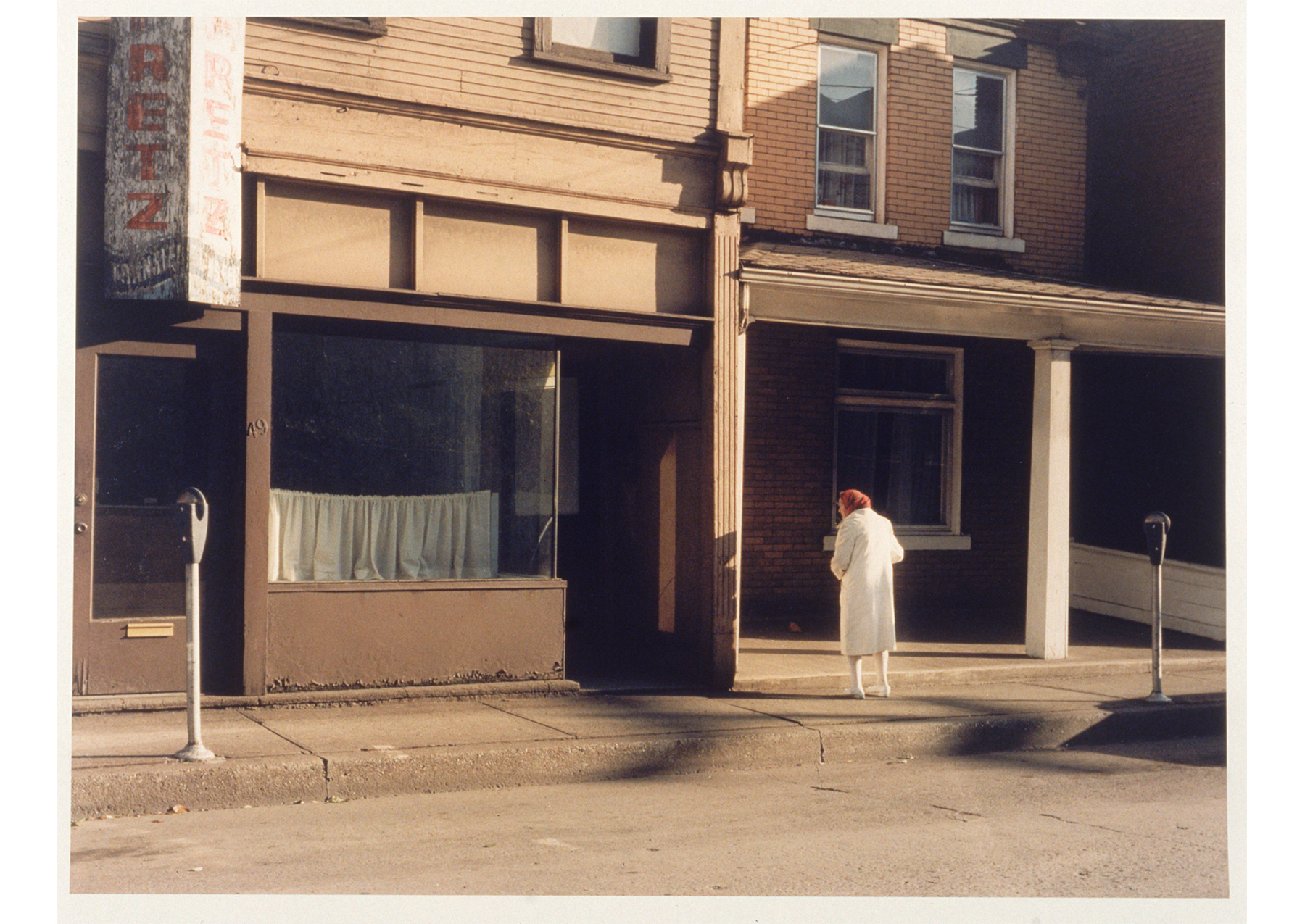 woman wearing a white coat stands in front of a storefront in the street