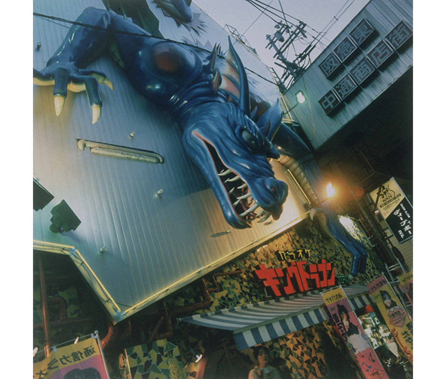 elaborately decorated modern building with blue and white striped awning, and giant blue dragon leaning down over front of building; several signs in Japanese