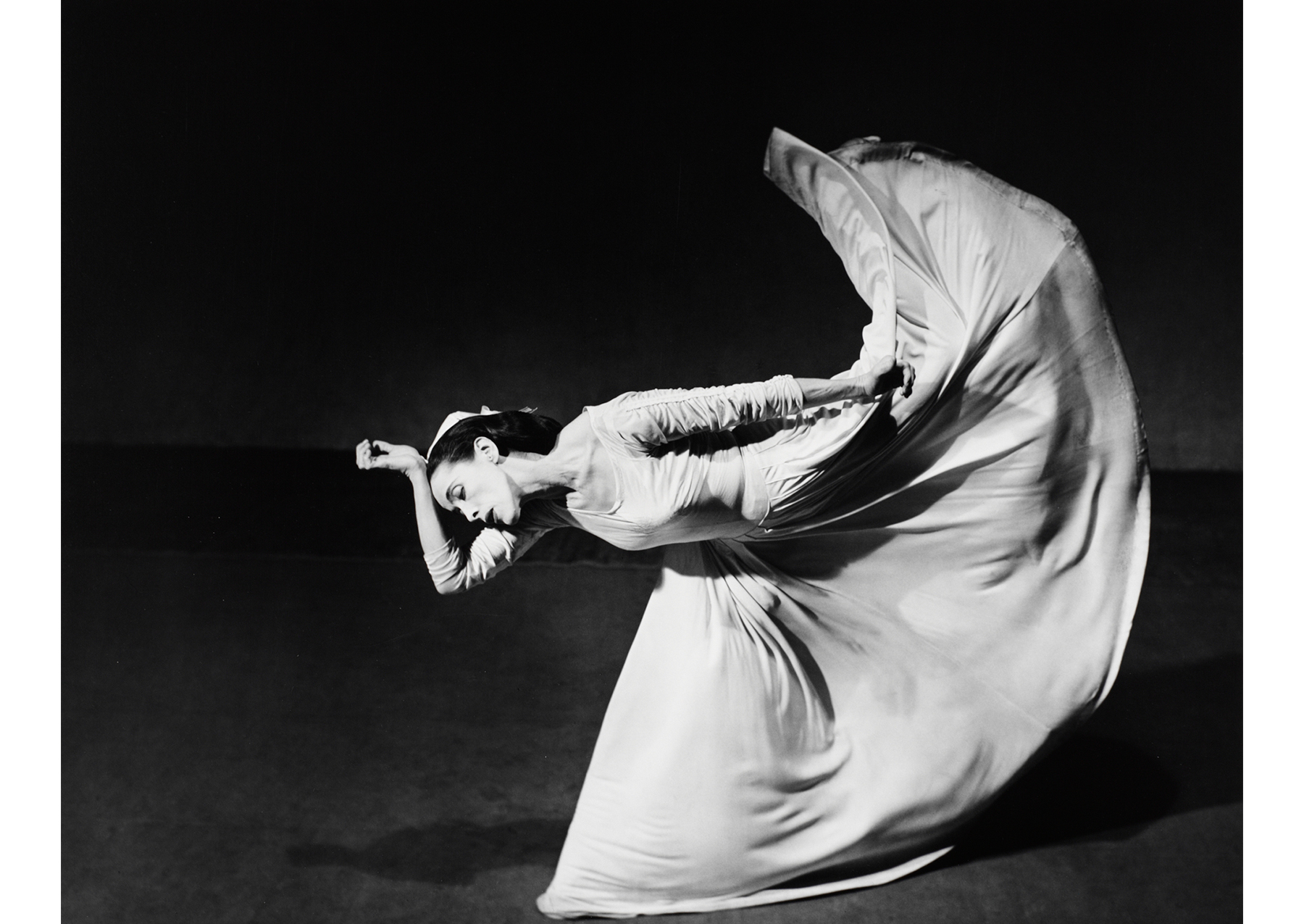 dancer in a full skirt, her body is parallel to the ground and ther left leg is lifted behind her