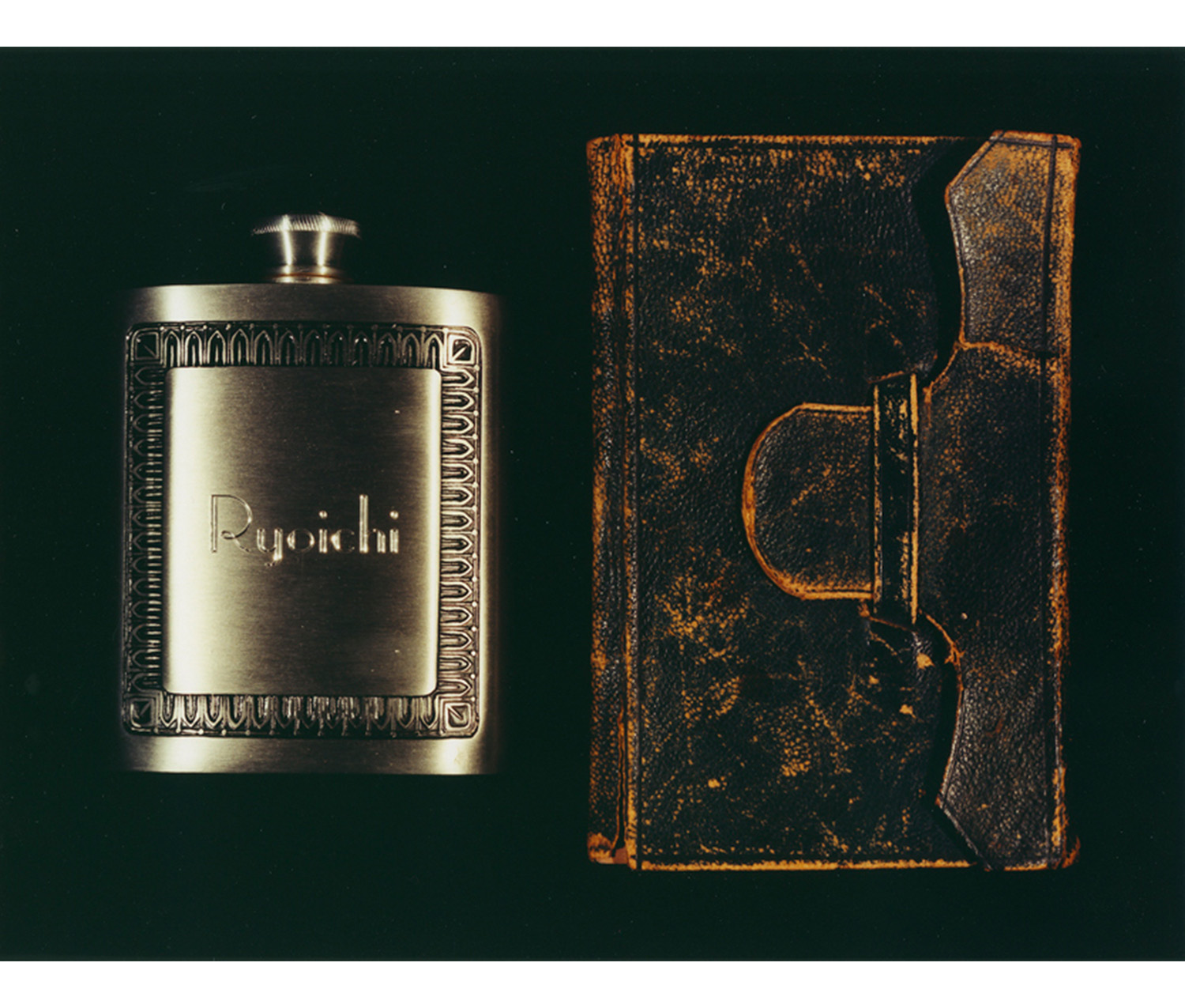 black background with image of metal flask on left embossed with Ryoichi and a designed frame around it, and small worn leather journal on right